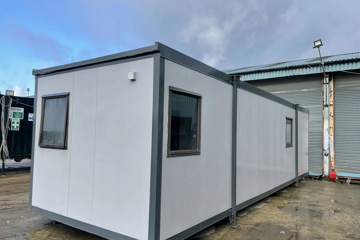 Used site office cabin standing in a yard with windows and a personnel door