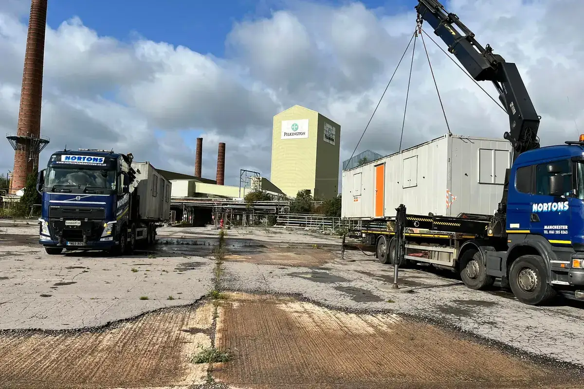 Temporary building being positioned on a prepared base beside a working factory