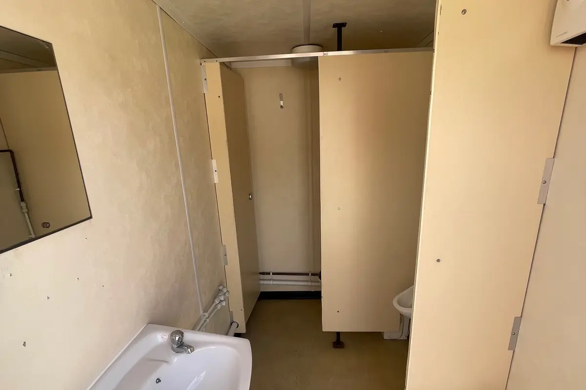 Inside a used toilet block showing cubicles and a wash basin